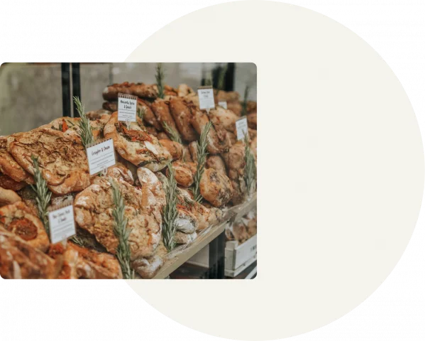 A grey square background has a round white circle in the center. To the left, there is a stock image of bread piled up on shelves with labels and rosemary around them.