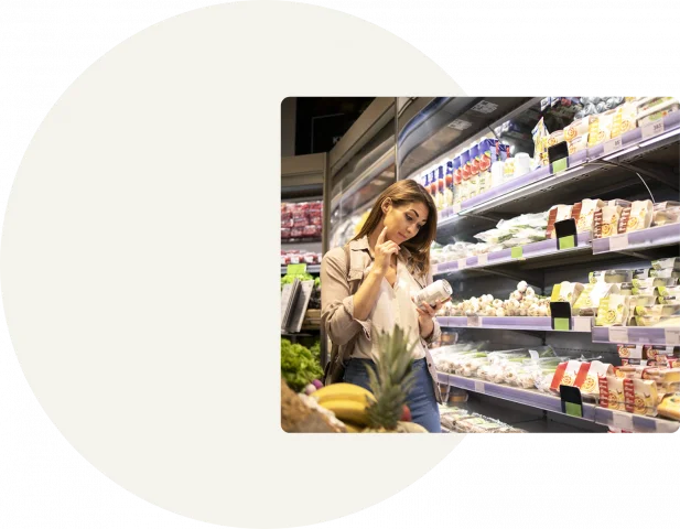 A square image shows a woman standing in a grocery store looking at a can and deciding whether to purchase it. The image is on a grey background with a white circle in the center of it.