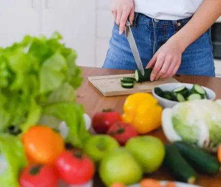 woman cutting cucumber on a table full of vegetables