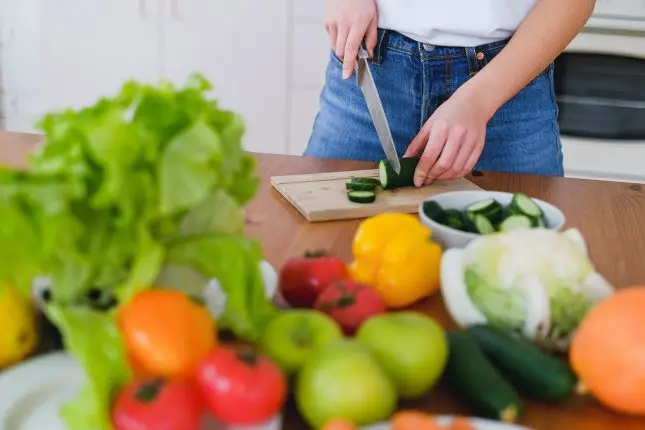 woman cutting cucumber on a table full of vegetables