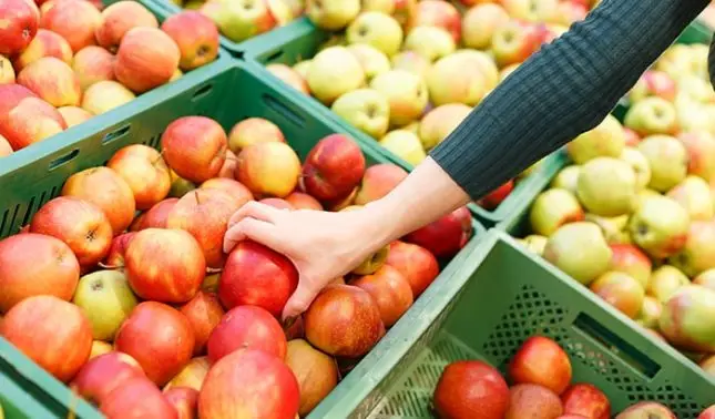 Close-up view of a woman's hand selecting an apple in a supermarket.